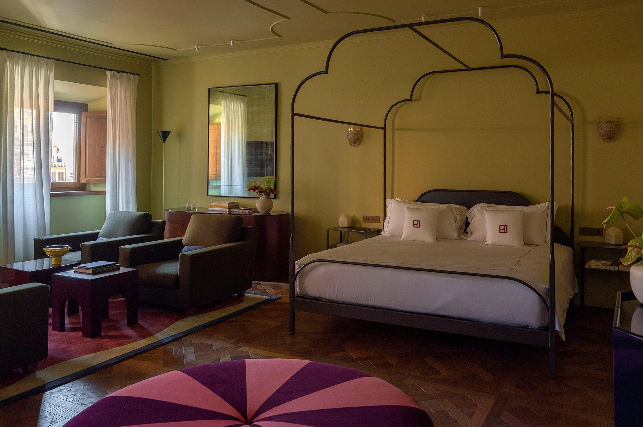 Ampia camera da letto padronale con letto a baldacchino in ferro battuto, divano, tappeto geometrico colorato e pareti verde salvia.