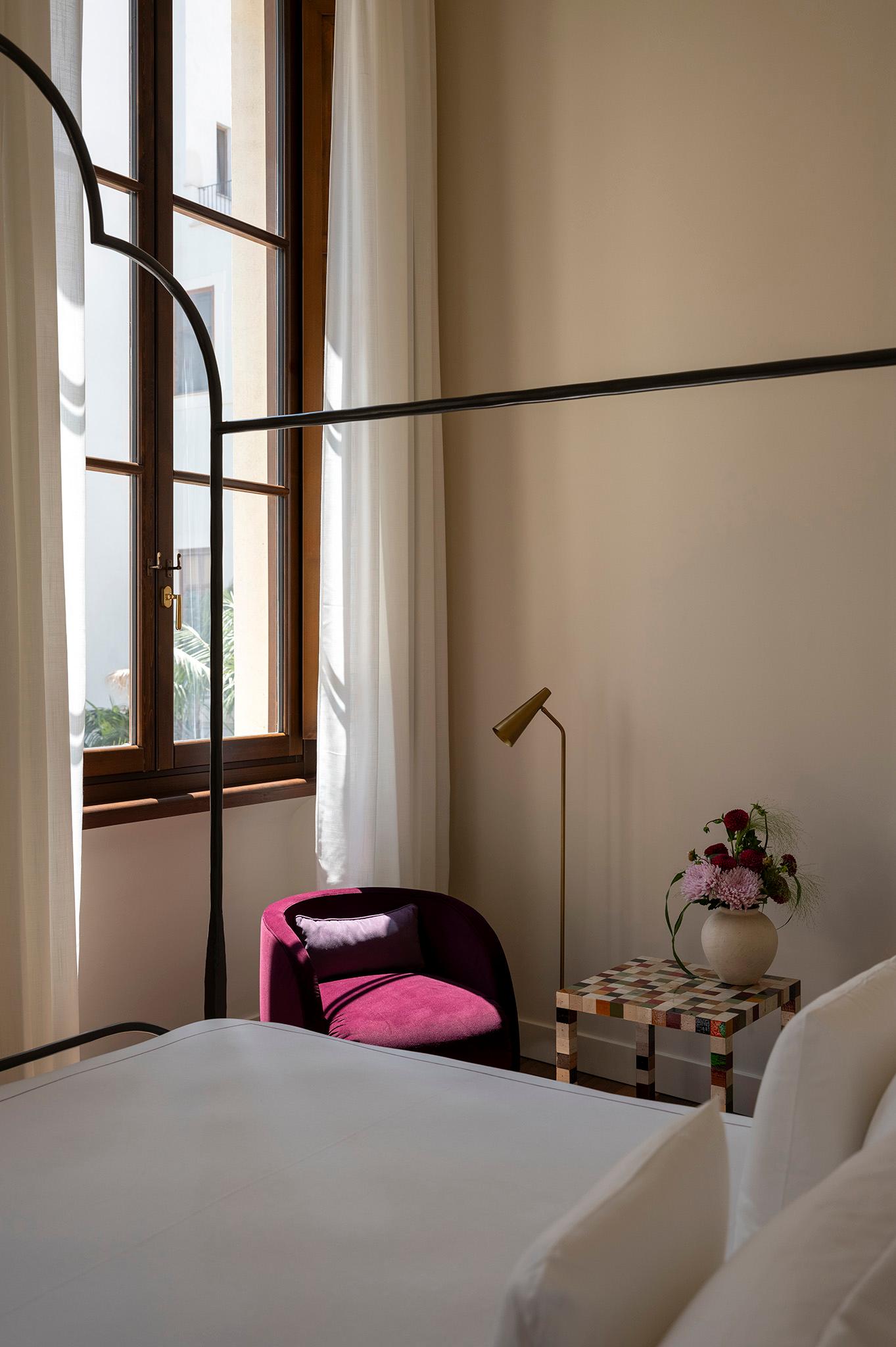Camera d'albergo elegante con letto matrimoniale, poltroncina in velluto rosa e un'ampia finestra luminosa.