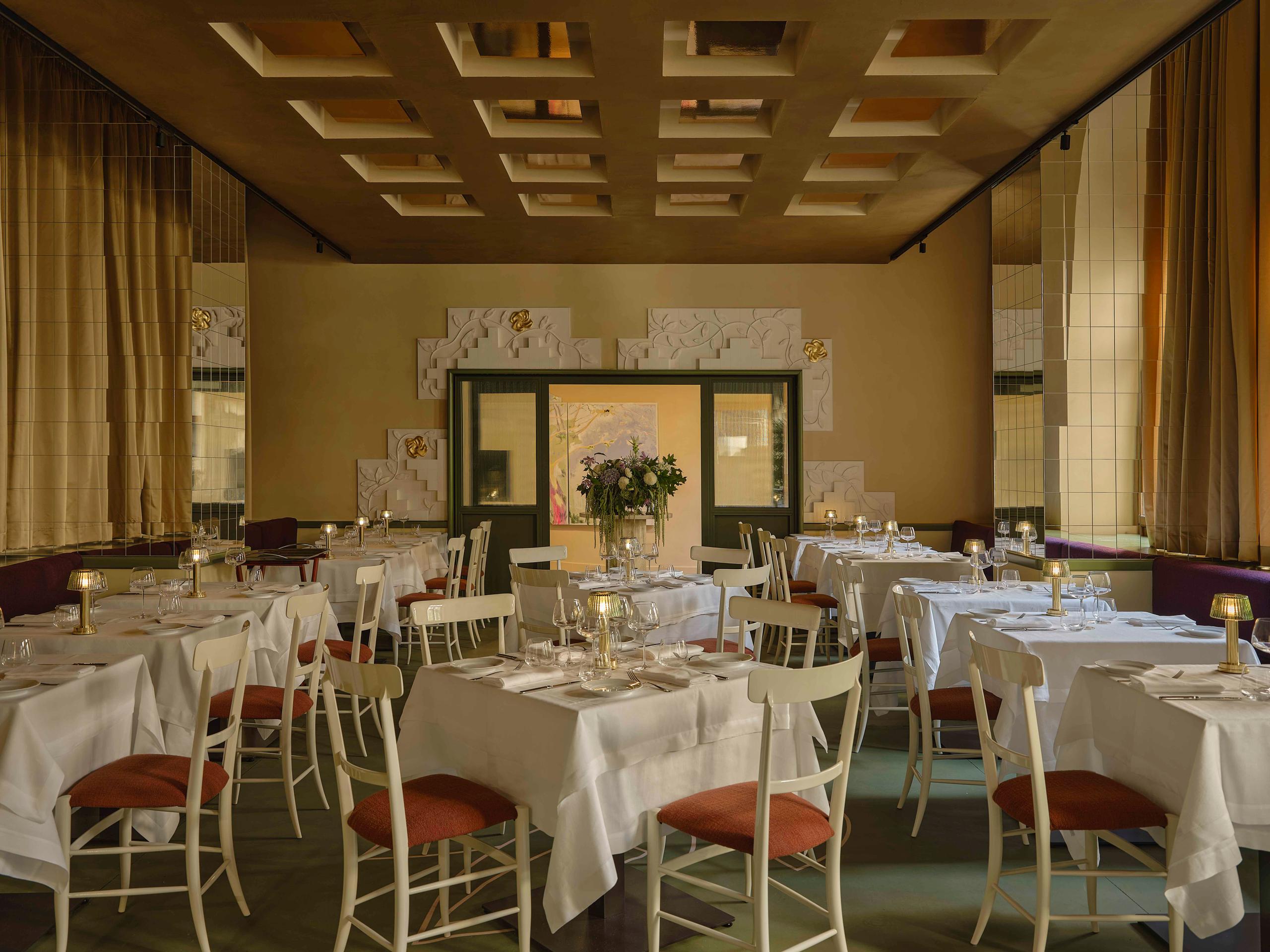 Sala ristorante raffinata con tavoli pronti, tovaglie bianche, soffitto geometrico e luci soffuse